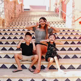 A mother and her two young children making silly faces for the camera while sitting on white and blue tiled stairs